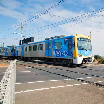 A train crosses the road as it arrives at Brighton Beach Railway Station, located on the Sandringham line in Victoria, Australia.