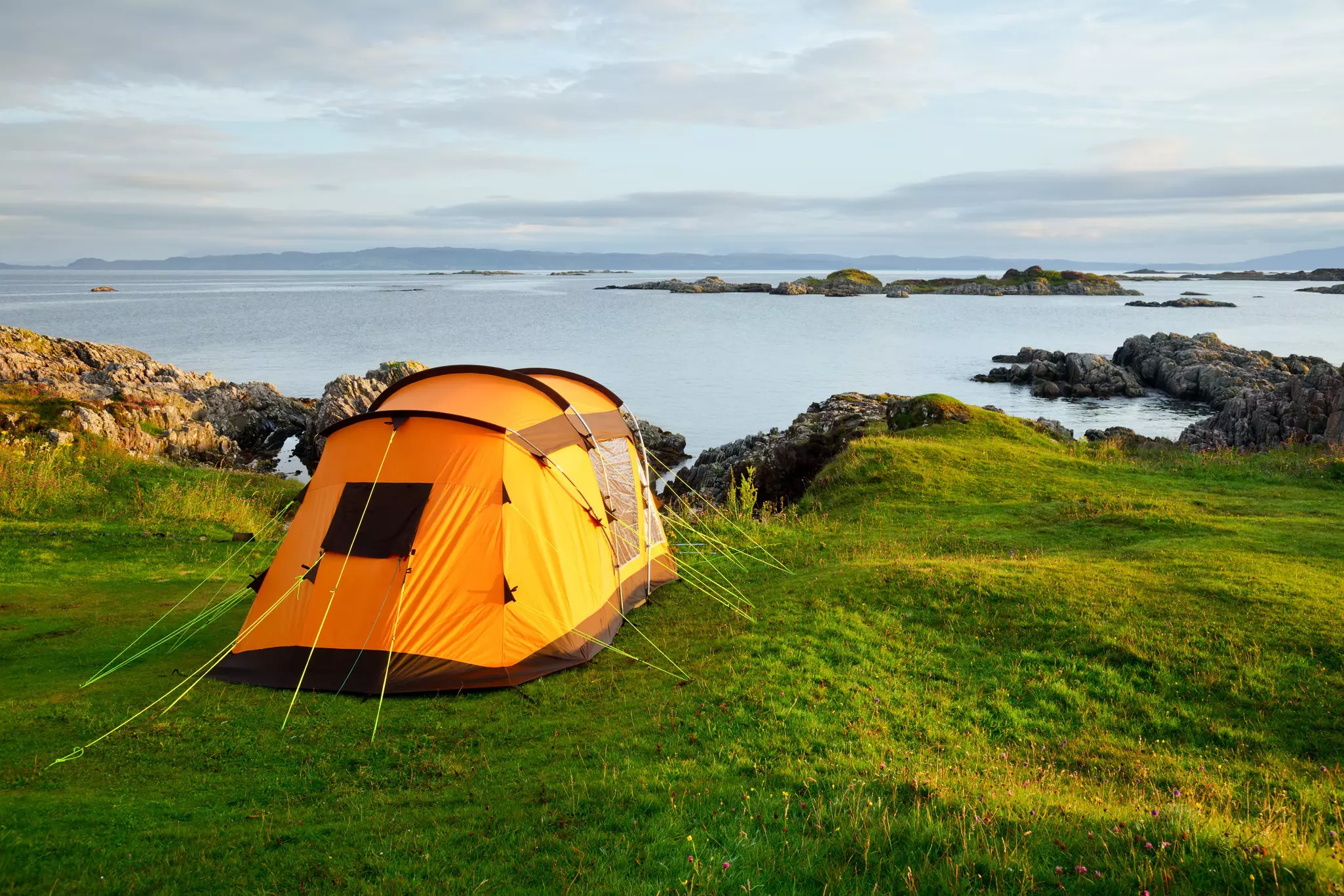 Orange camping tent on a shore in a morning light