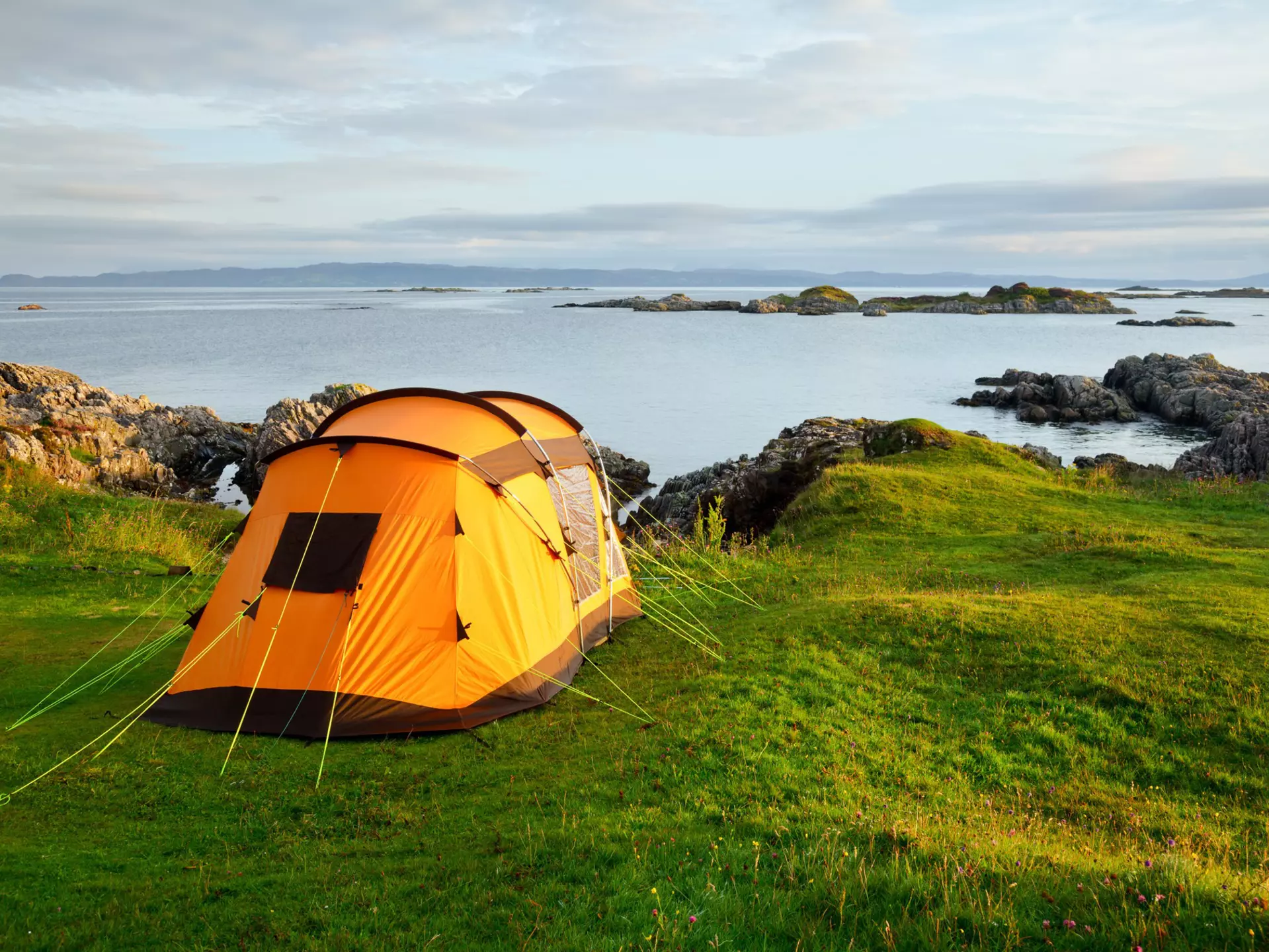 Orange camping tent on a shore in a morning light