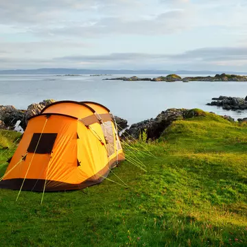 Orange camping tent on a shore in a morning light