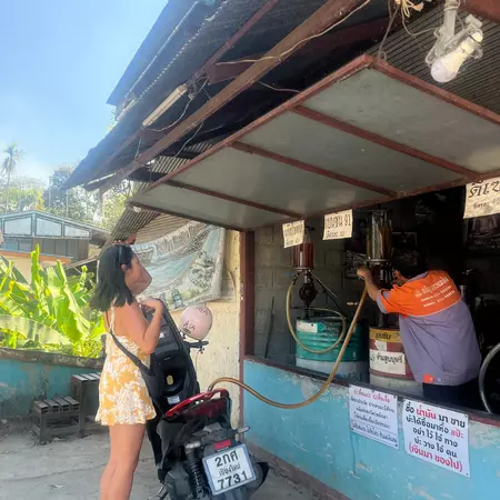 A woman stops at a kiosk selling fuel to refill the tank of her scooter.