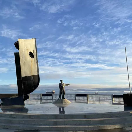 A statue at the edge of the ocean points towards the sea