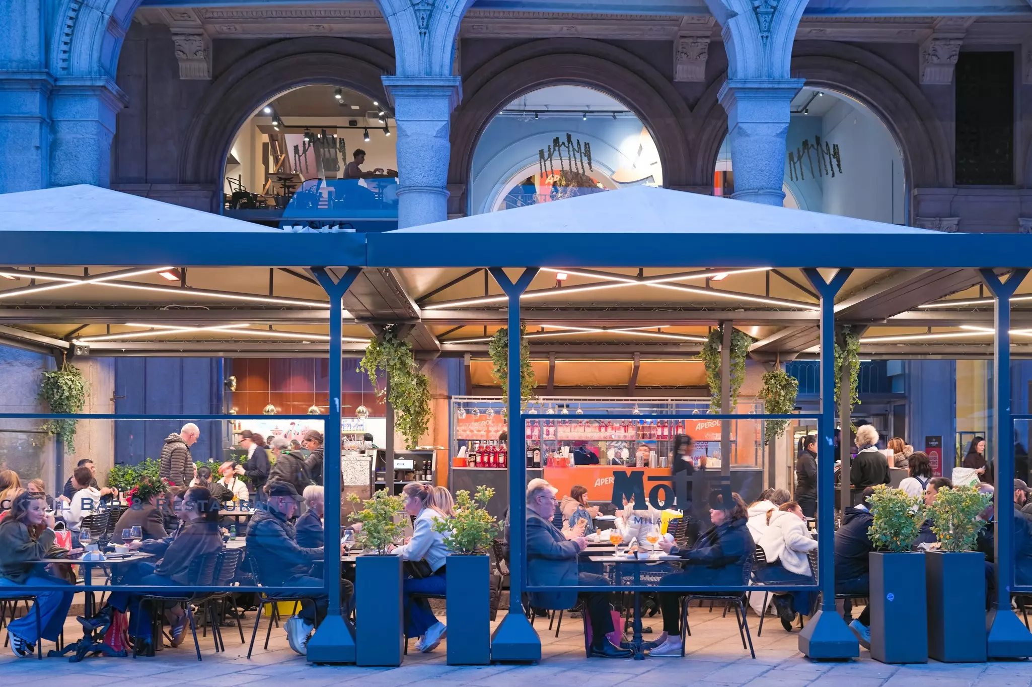 People sit at outdoor tables at a cafe on a stylish city street.