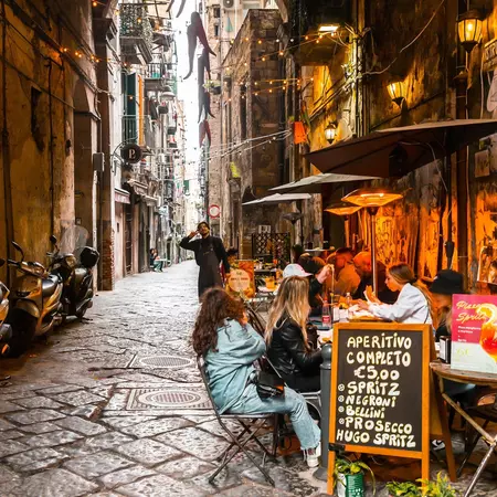 People sit at tables on a narrow street.
