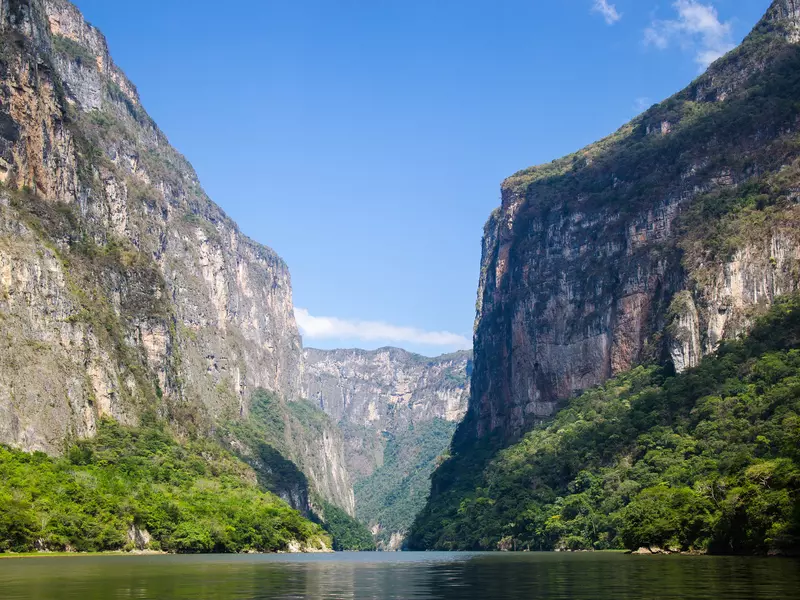 A body of water in a canyon surrounded by tall, rocky mountains on a sunny day.