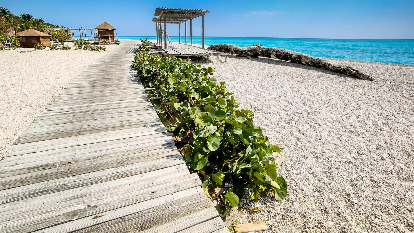A wooden boardwalk above a pebbly beach leads to a small shelter.