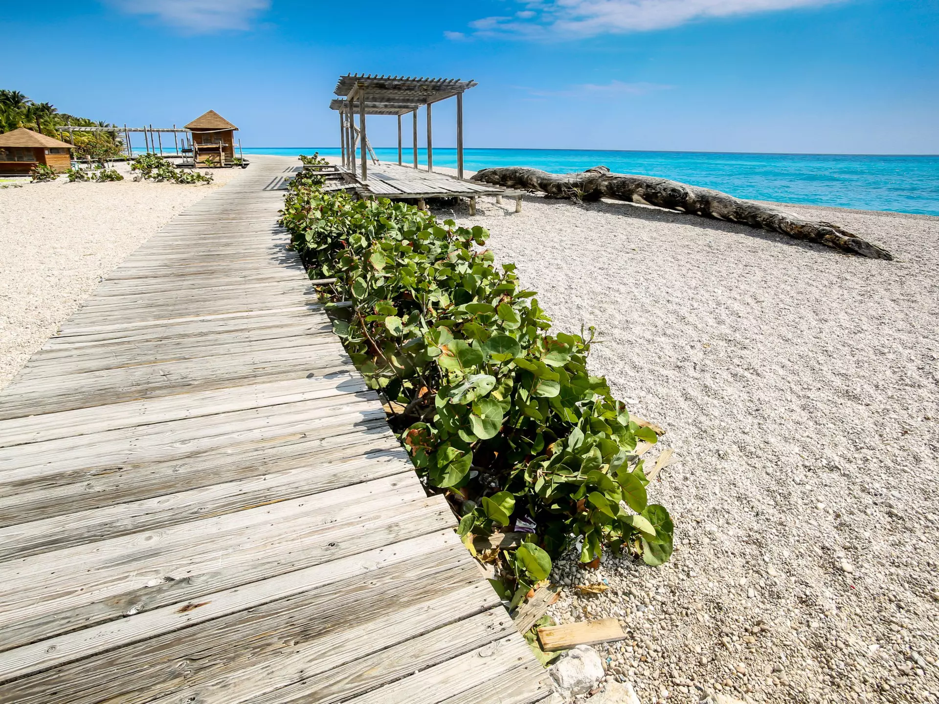 A wooden boardwalk above a pebbly beach leads to a small shelter.