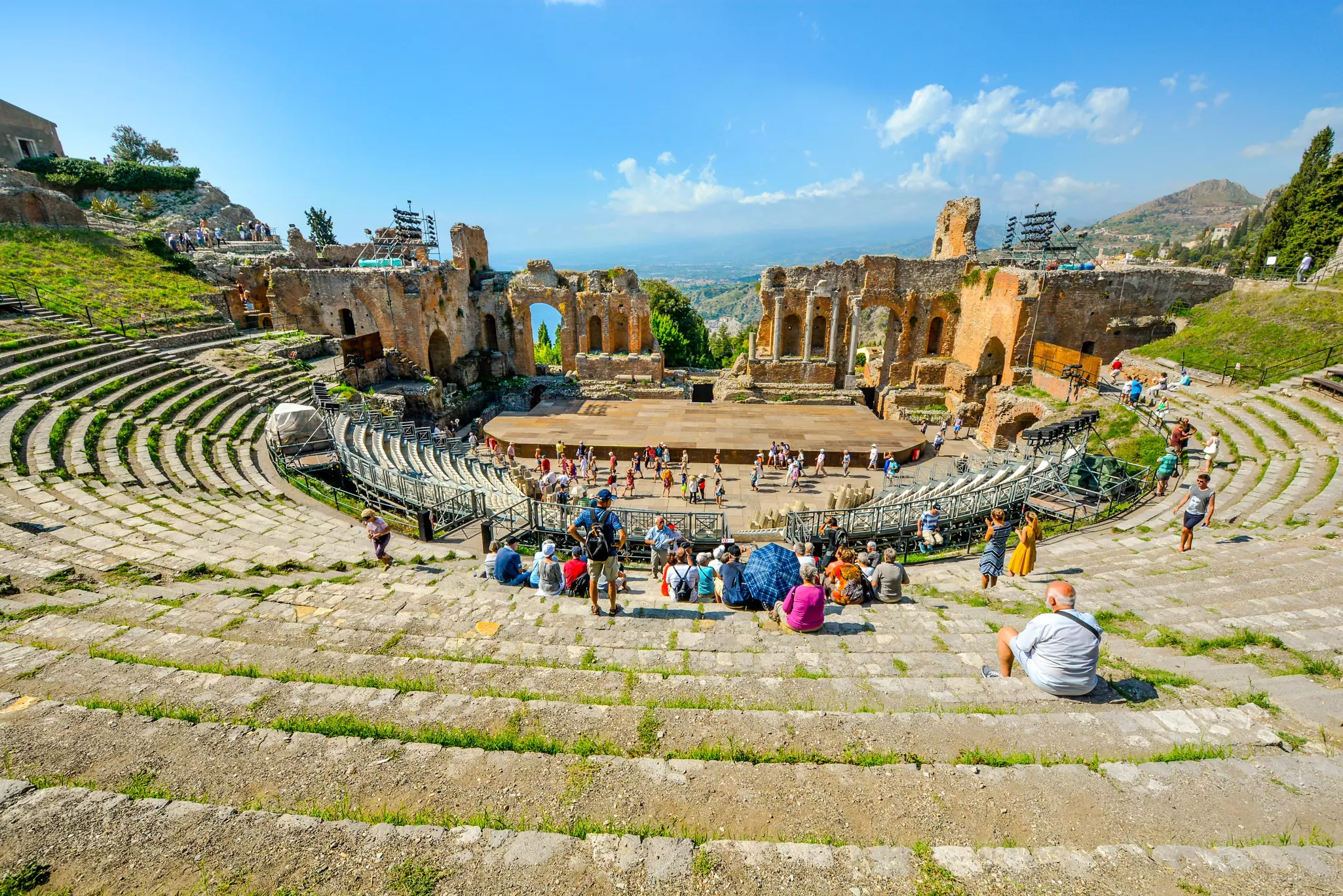 Visitors sit and mill around the ruins of an ancient Greek theater