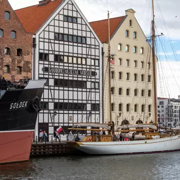 Black-hulled ship and a white sailing schooner docked in front of brick and half-timbered buildings with a museum sign