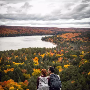 Couple sitting on a rock, overlooking a forest of fall colors and a lake in Algonquin Provincial Park, Canada