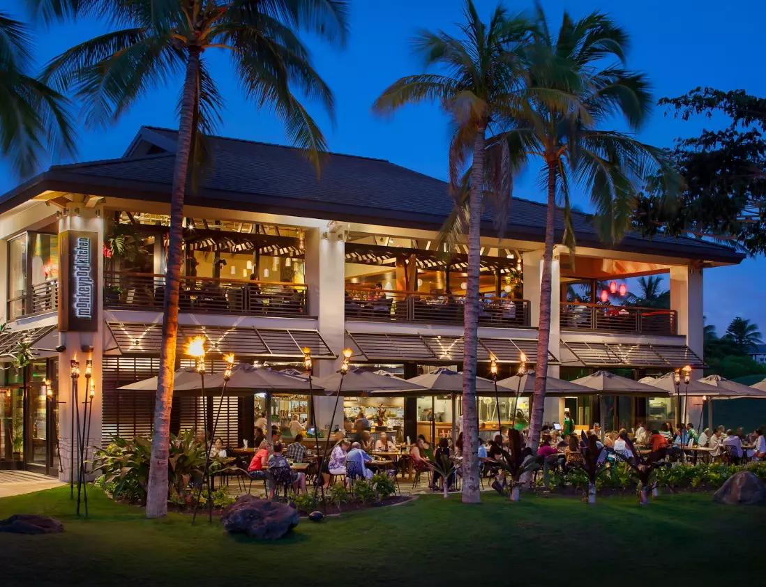 Evening diners at tables under palm trees at the two-story Monkeypod Kitchen at the Ko Olina Center
