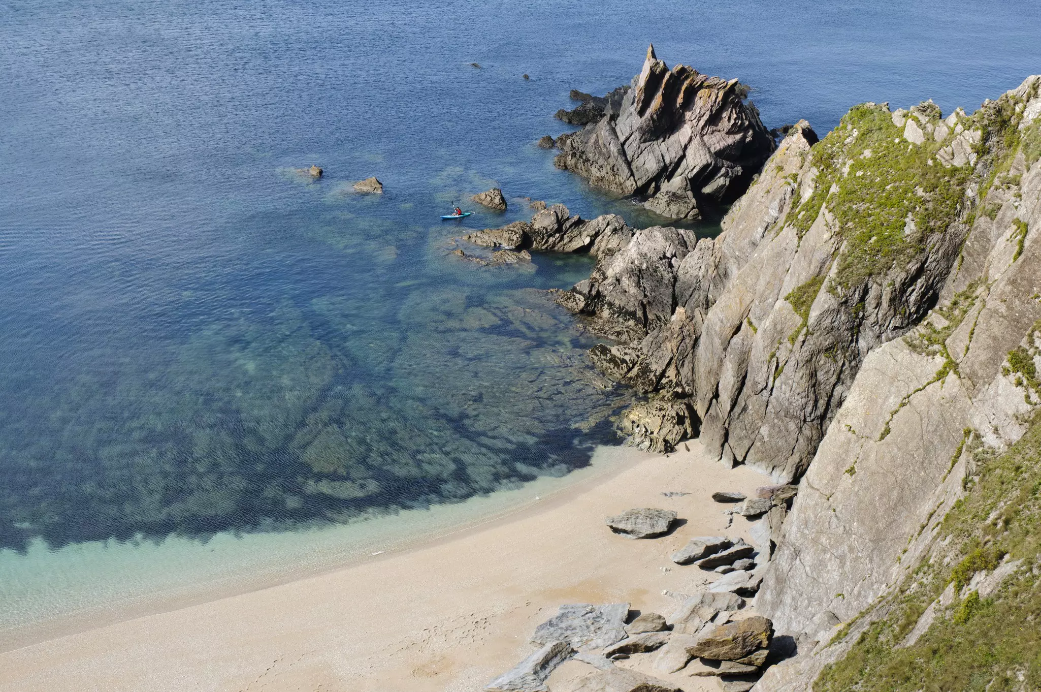Beautiful clear water, beach and cliffs in south Devon, England, with small sea kayak visible.