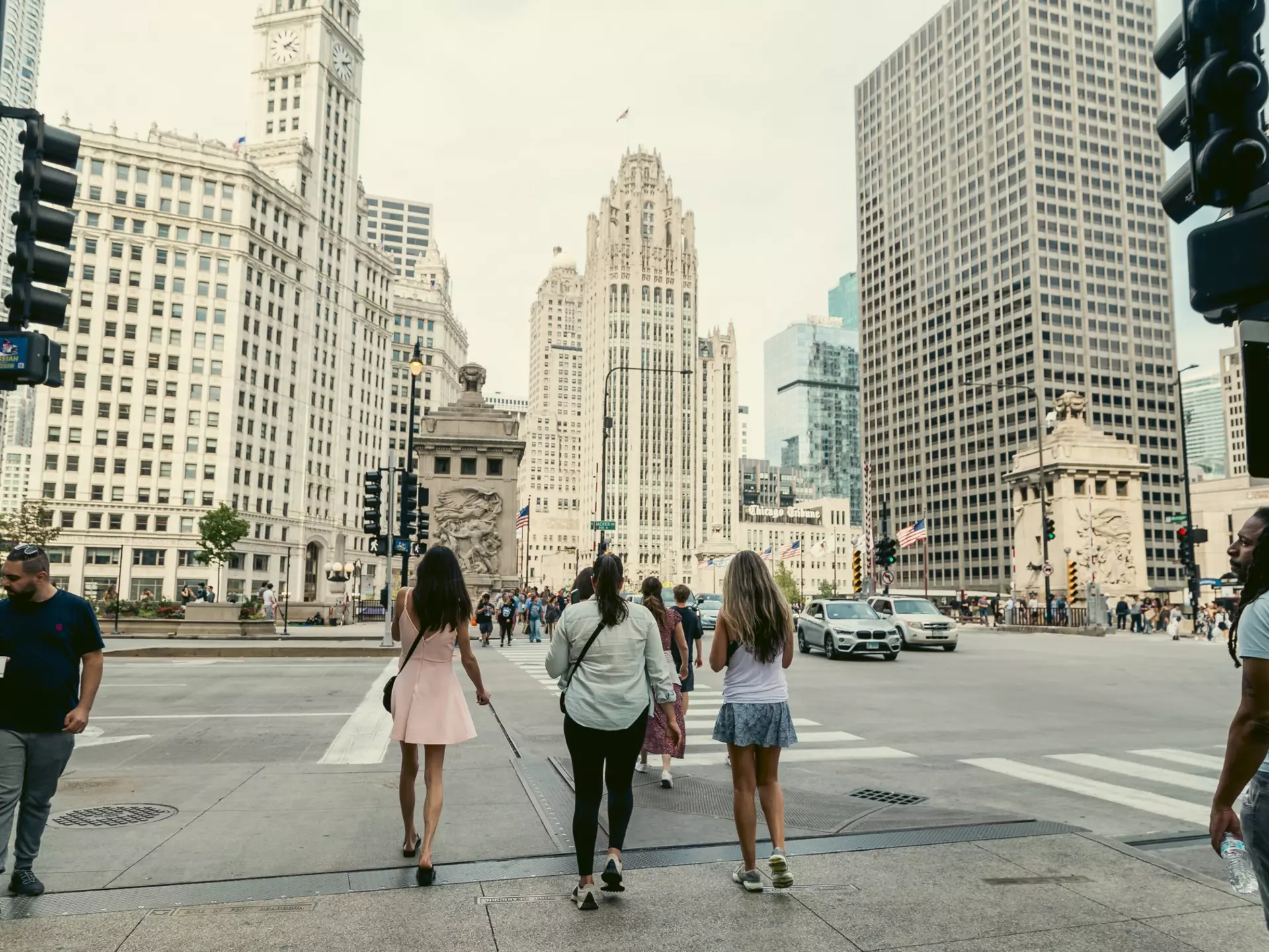 People walk across a crosswalk in the direction of a tall white skyscraper.
