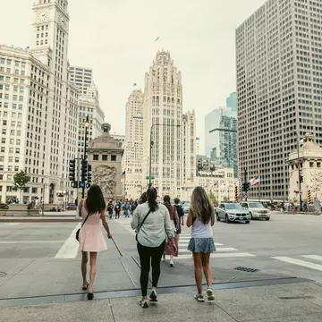 People walk across a crosswalk in the direction of a tall white skyscraper.