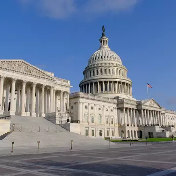 Columned portico and wide marble steps below the statue-topped dome; a US flag over an empty stone plaza.