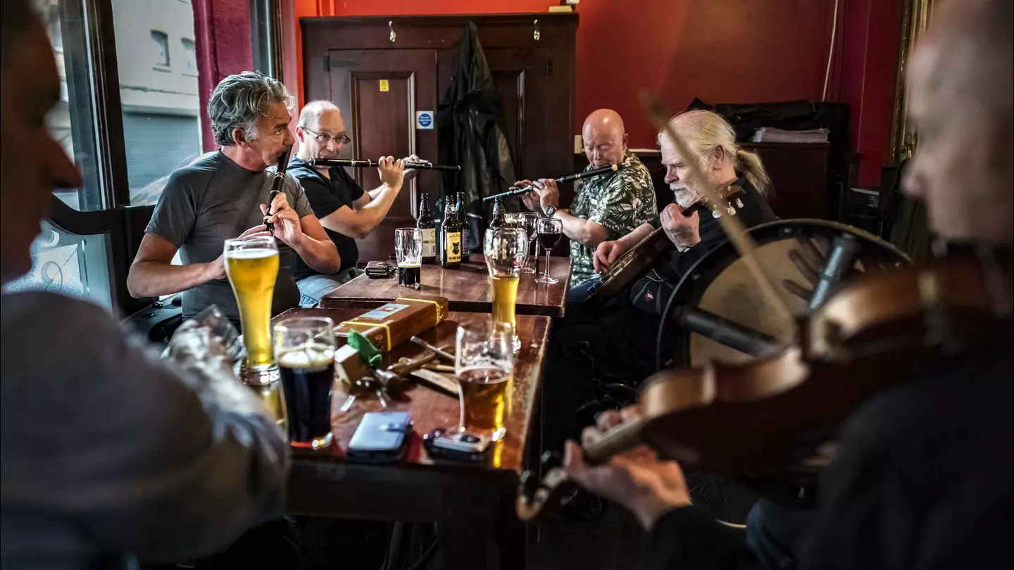 Musicians perform while seated around a table at a pub in Belfast.