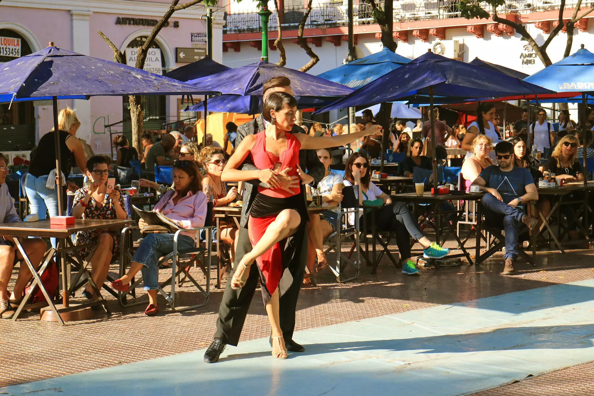 Two tango dancers perform in front of a cafe terrace filled with people