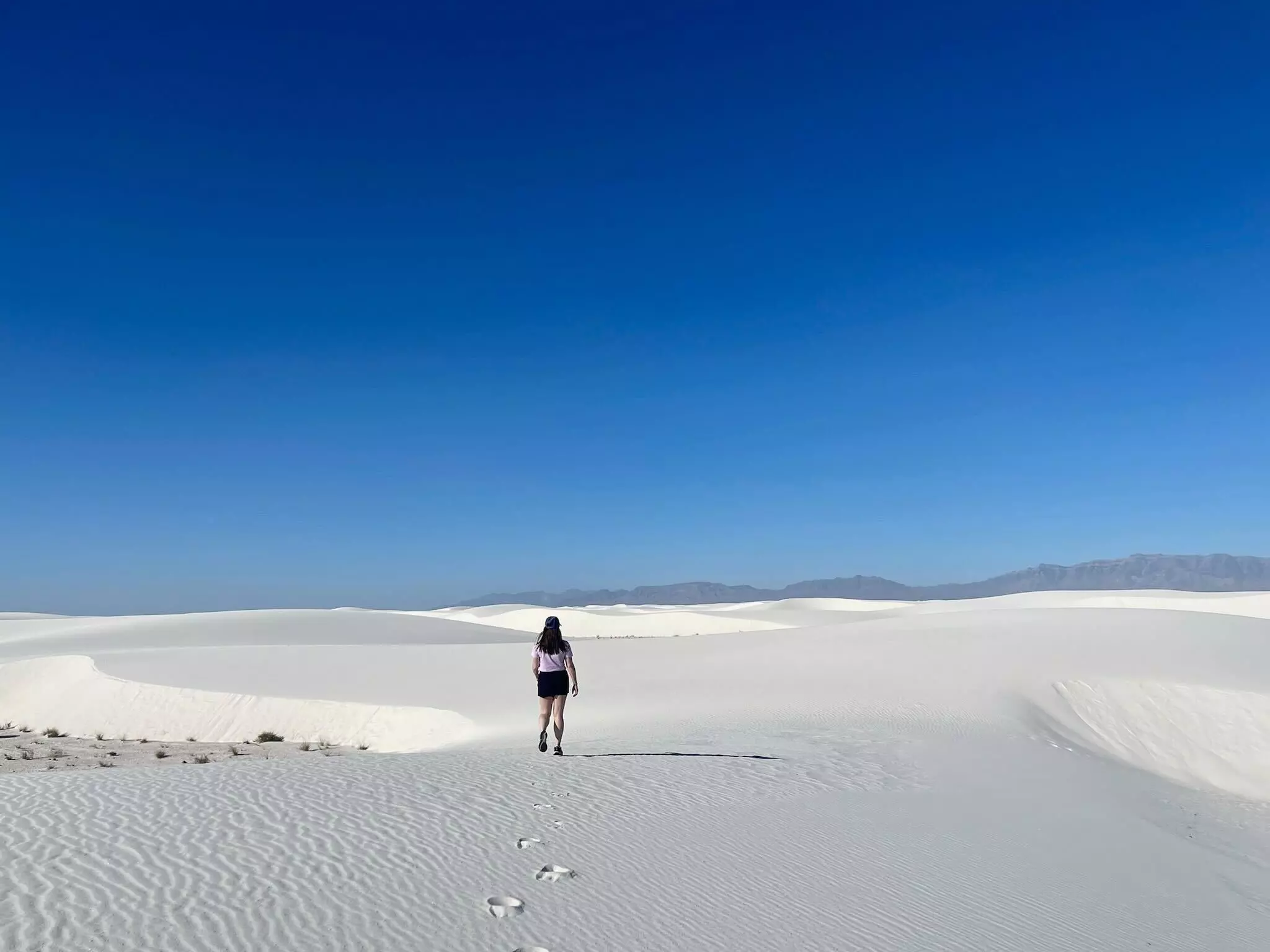A woman walks through the white sand dunes of a national park.