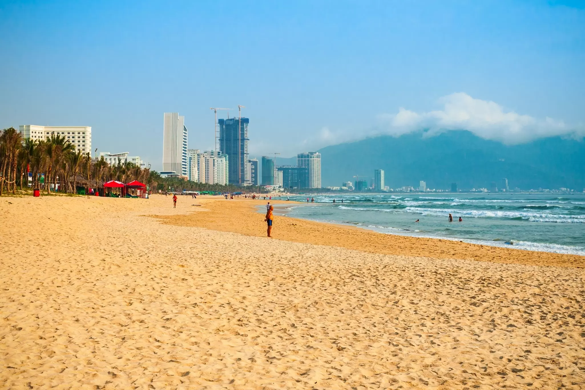 A wide, long beach has only a few people, with a view of a city skyline in the distance, Danang, Vietnam