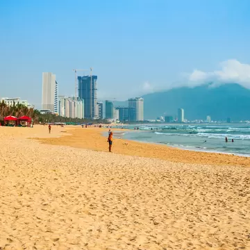 A wide, long beach has only a few people, with a view of a city skyline in the distance, Danang, Vietnam