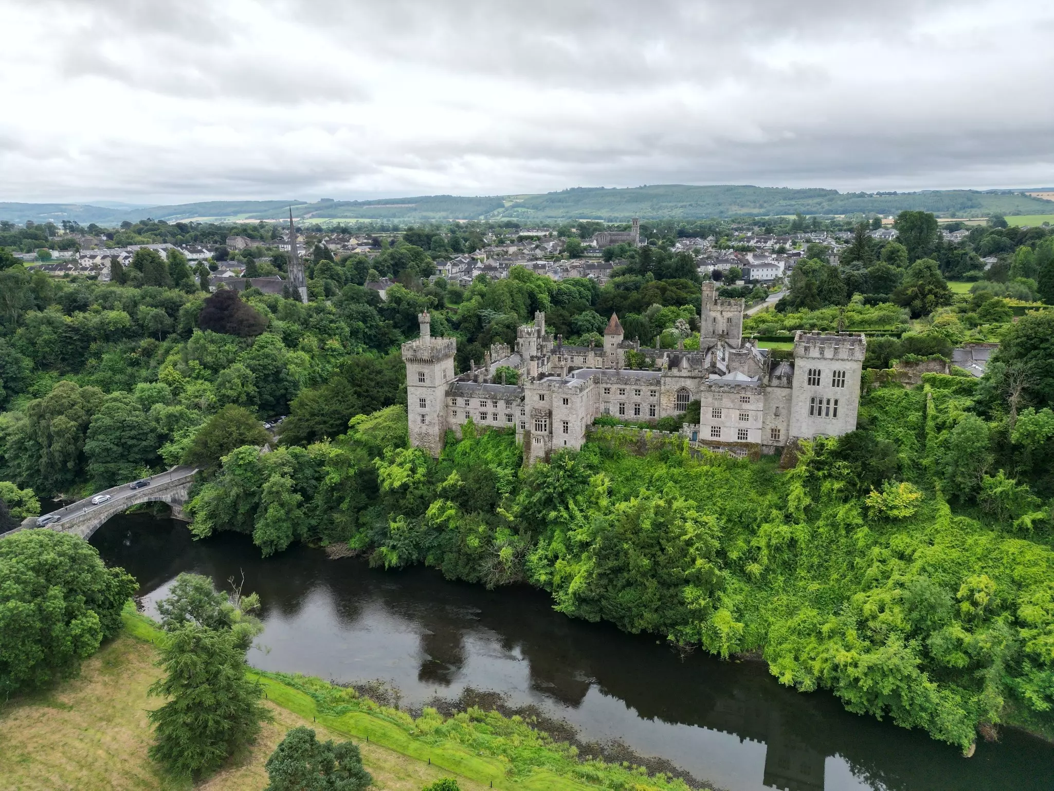 A castle surrounded by trees, with a river and a small village nearby.