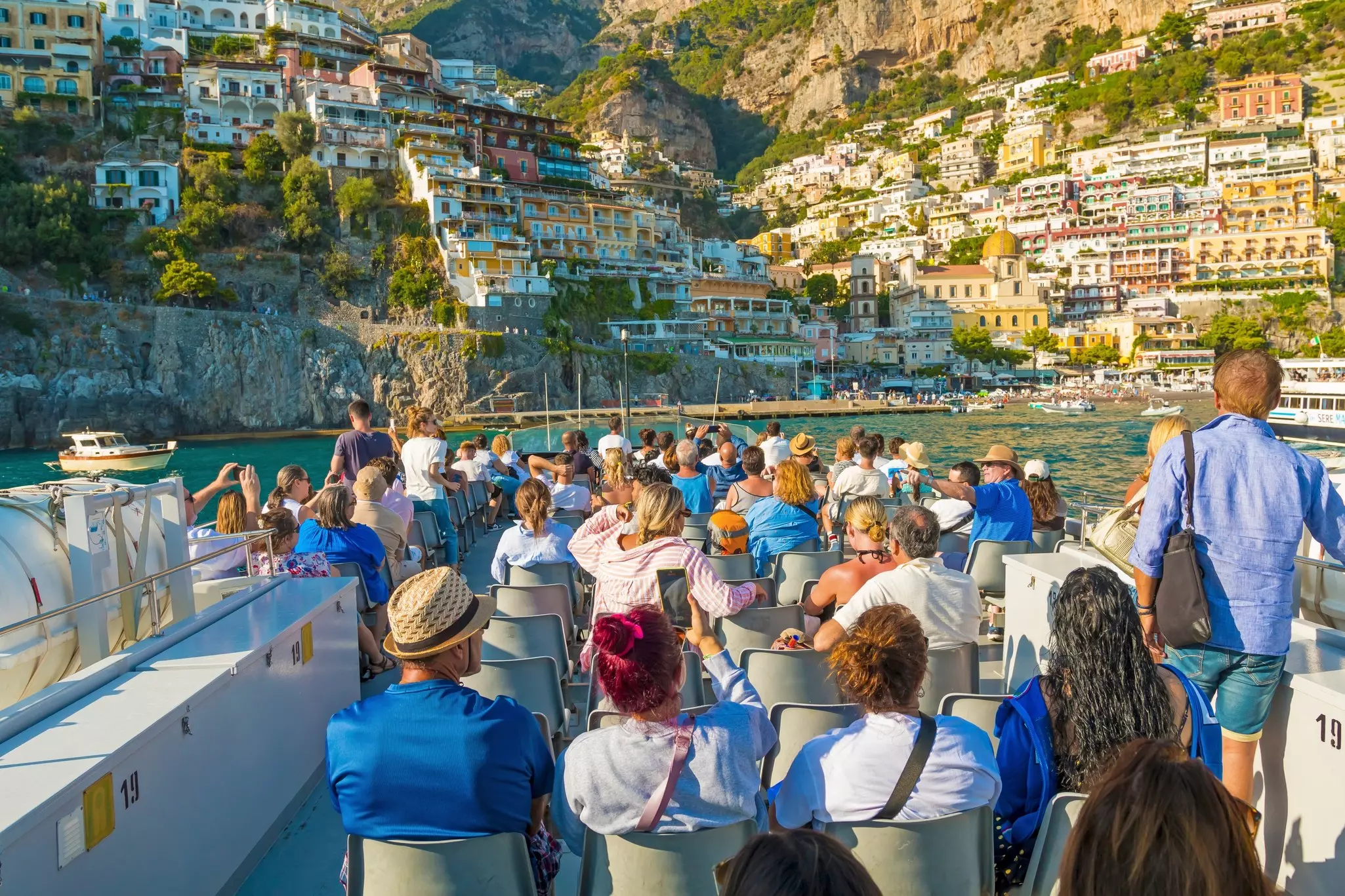 Tourists on a ferry boat near Positano on the Amalfi Coast, enjoying stunning views of colorful cliffside houses, turquoise waters, and the picturesque coastline.