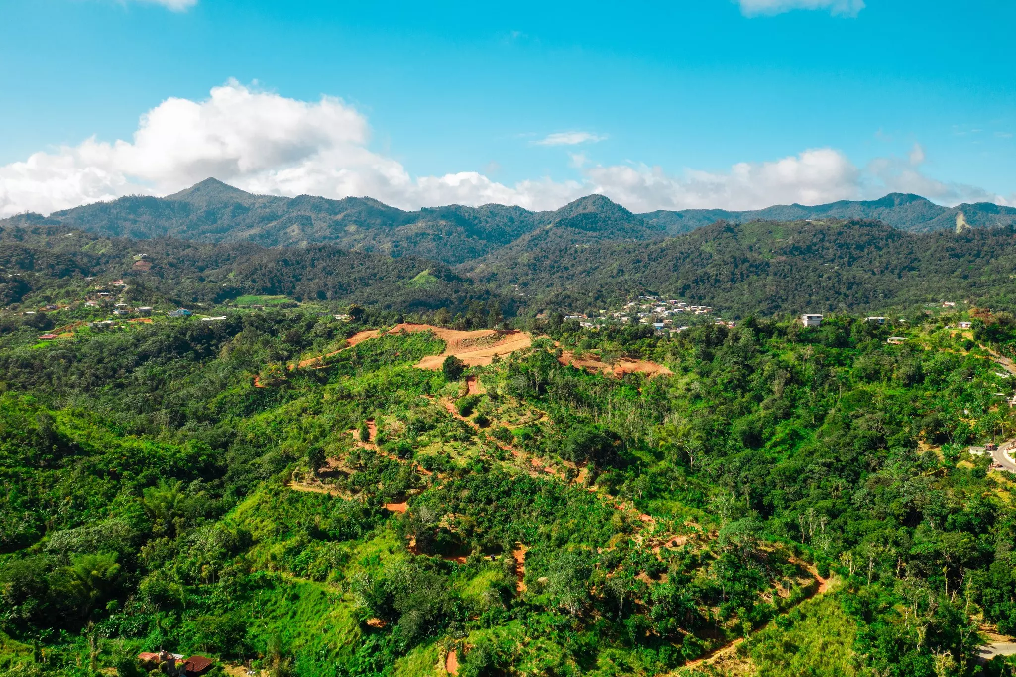 An aerial view of a mountain landscape with forest in the foreground on a bright, sunny day.