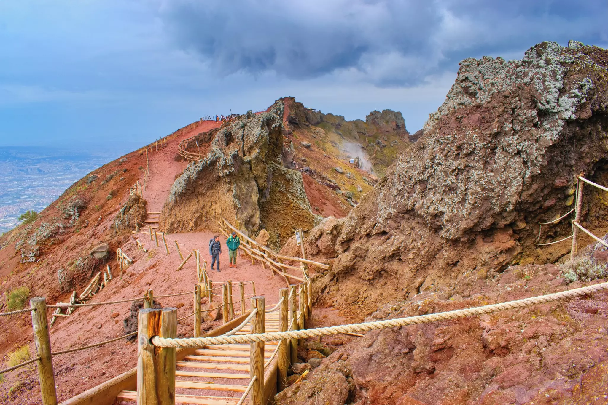 Two hikers follow a marked trail through a red rocky landscape