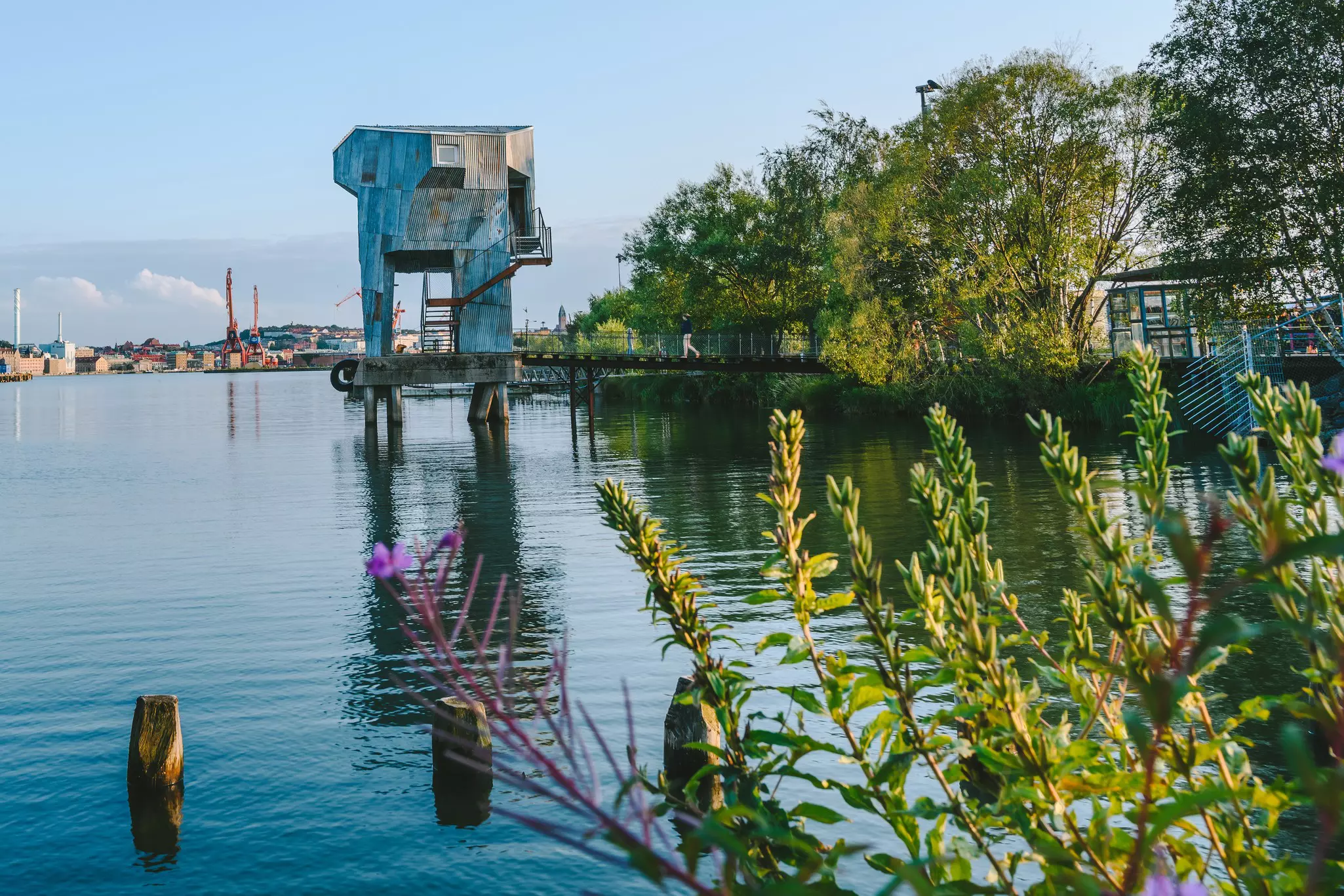 A large wooden structure stands in a harbor with steps up to a sauna at the top