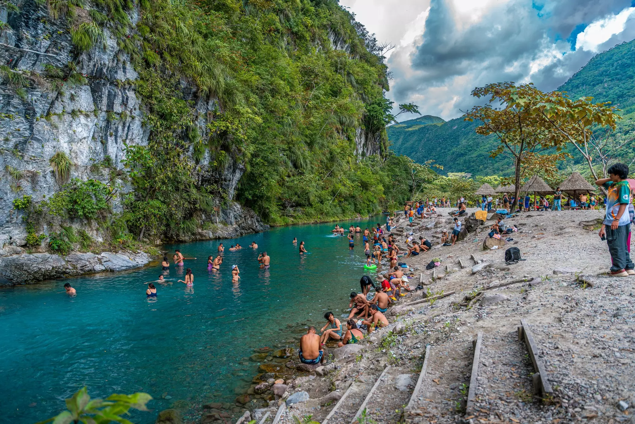 A busy riverside with people paddling and swimming in the jungle.