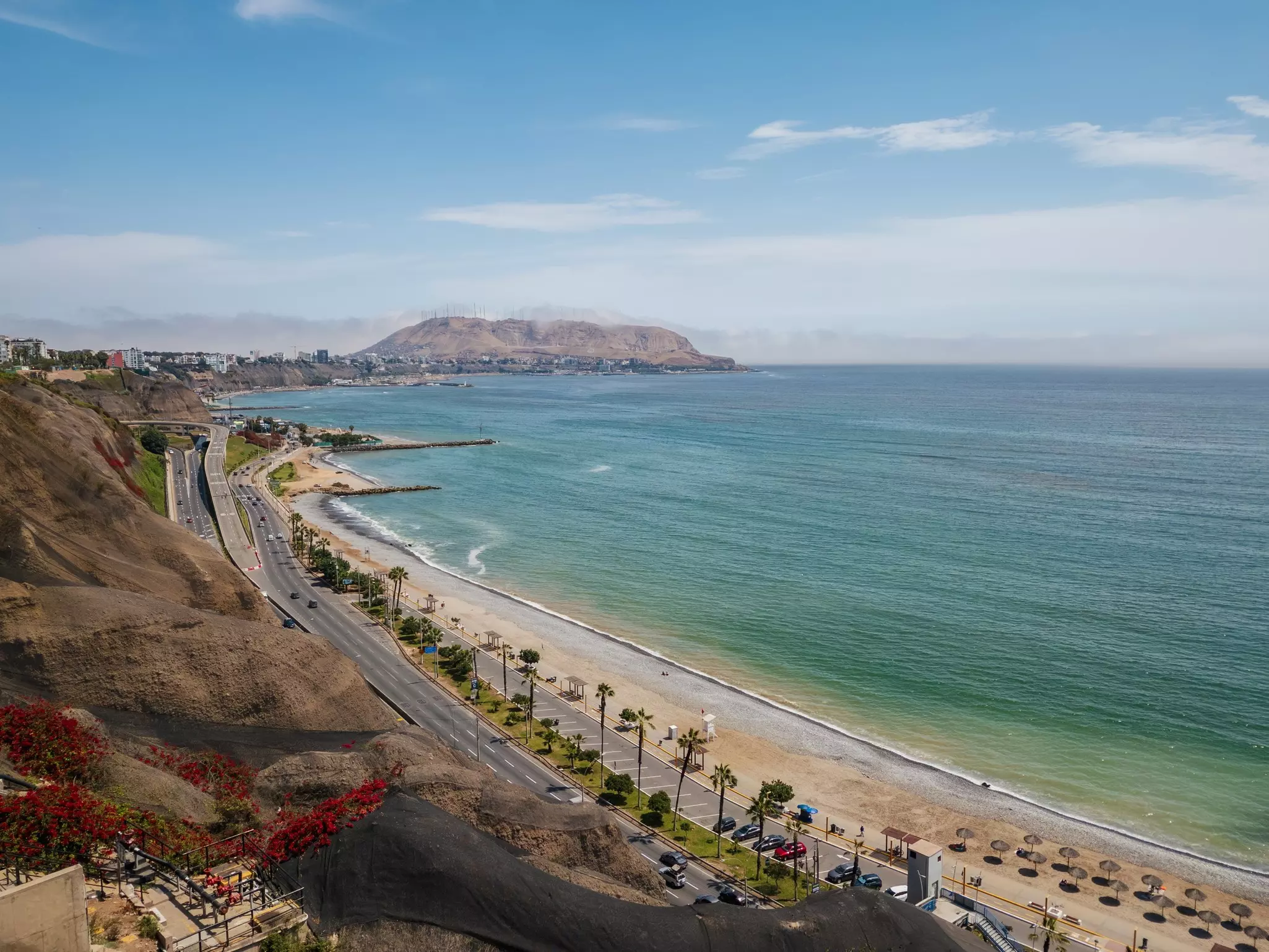 A long sandy beach, with a dry mountain in the distance.