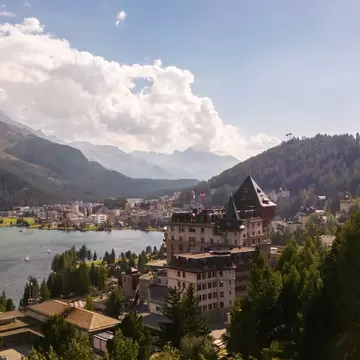 A tall, brown building overlooking a body of water and a verdant mountainside in Switzerland