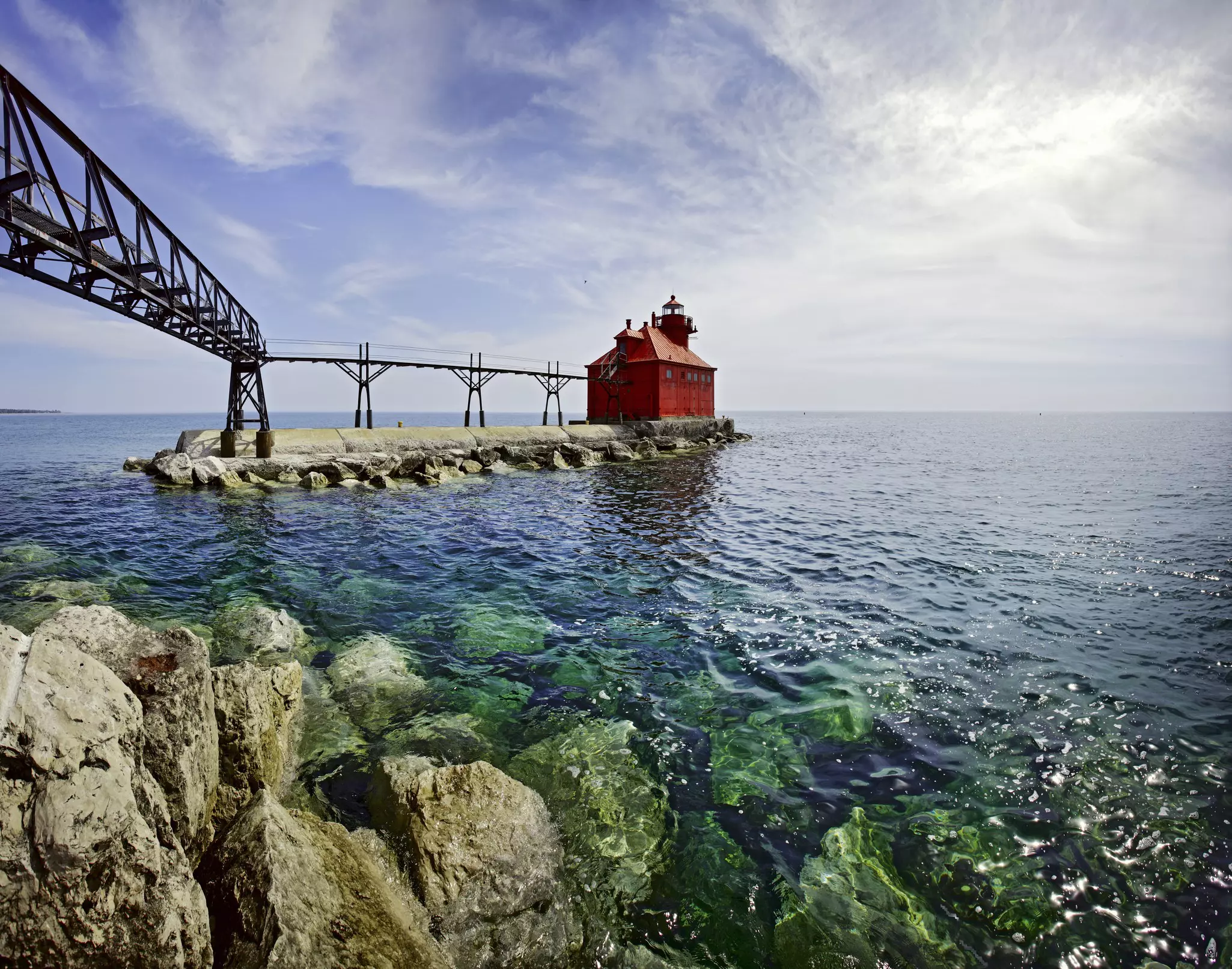 A red, squat lighthouse building at the edge of pier leading into a lake