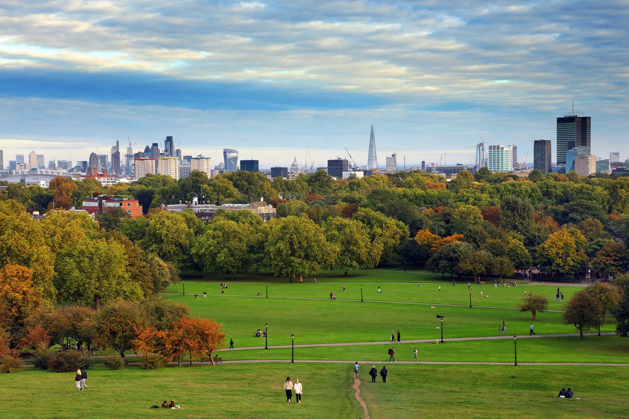 People walk around the grass on Primrose Hill in Regent's Park during the late afternoon.