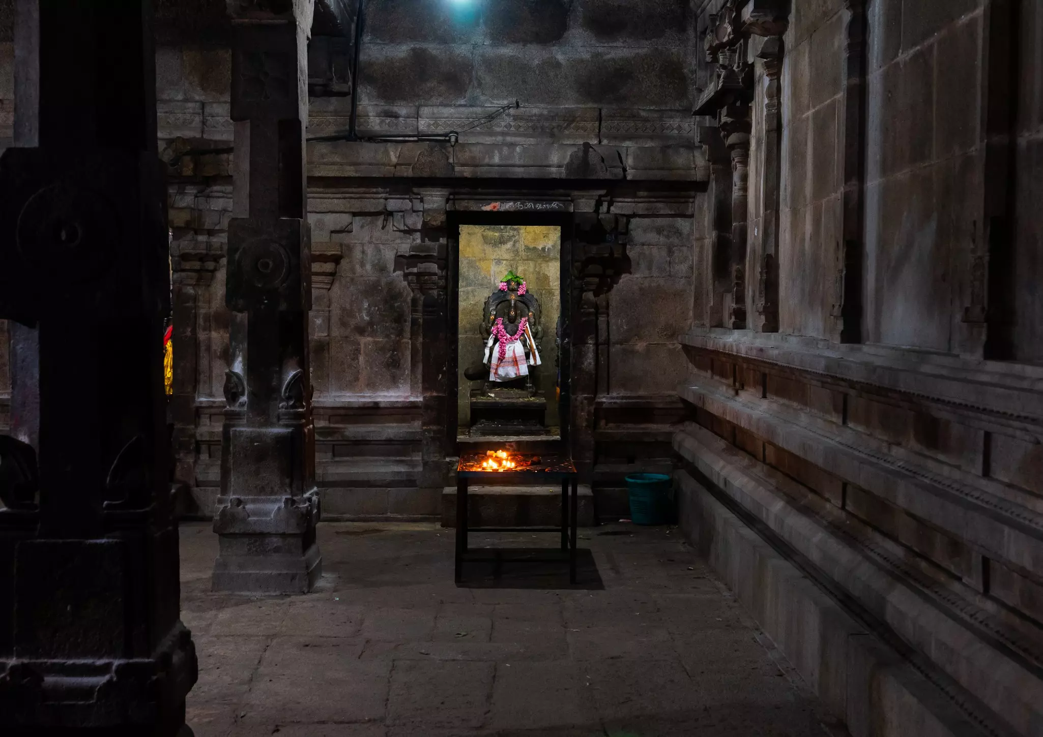 Candles burn in front of an effigy of a god in a rock-cut temple.
