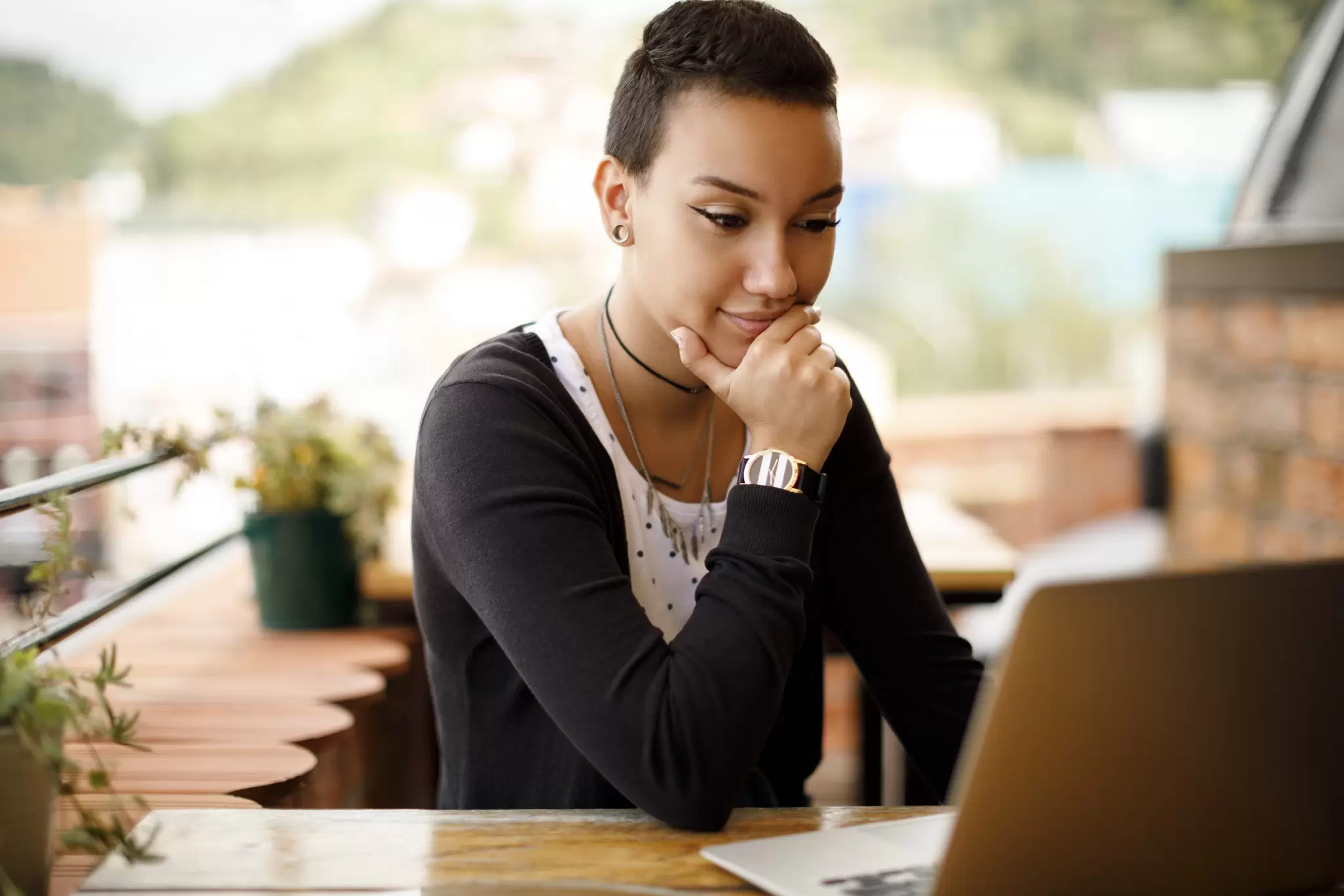 Young woman working on a laptop at an outdoor cafe table overlooking a hillside town
