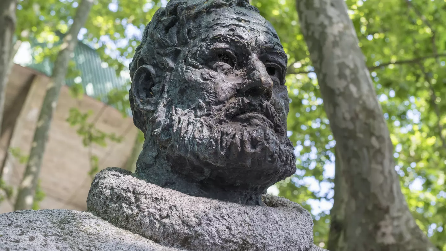 A statue of a bearded man under trees.