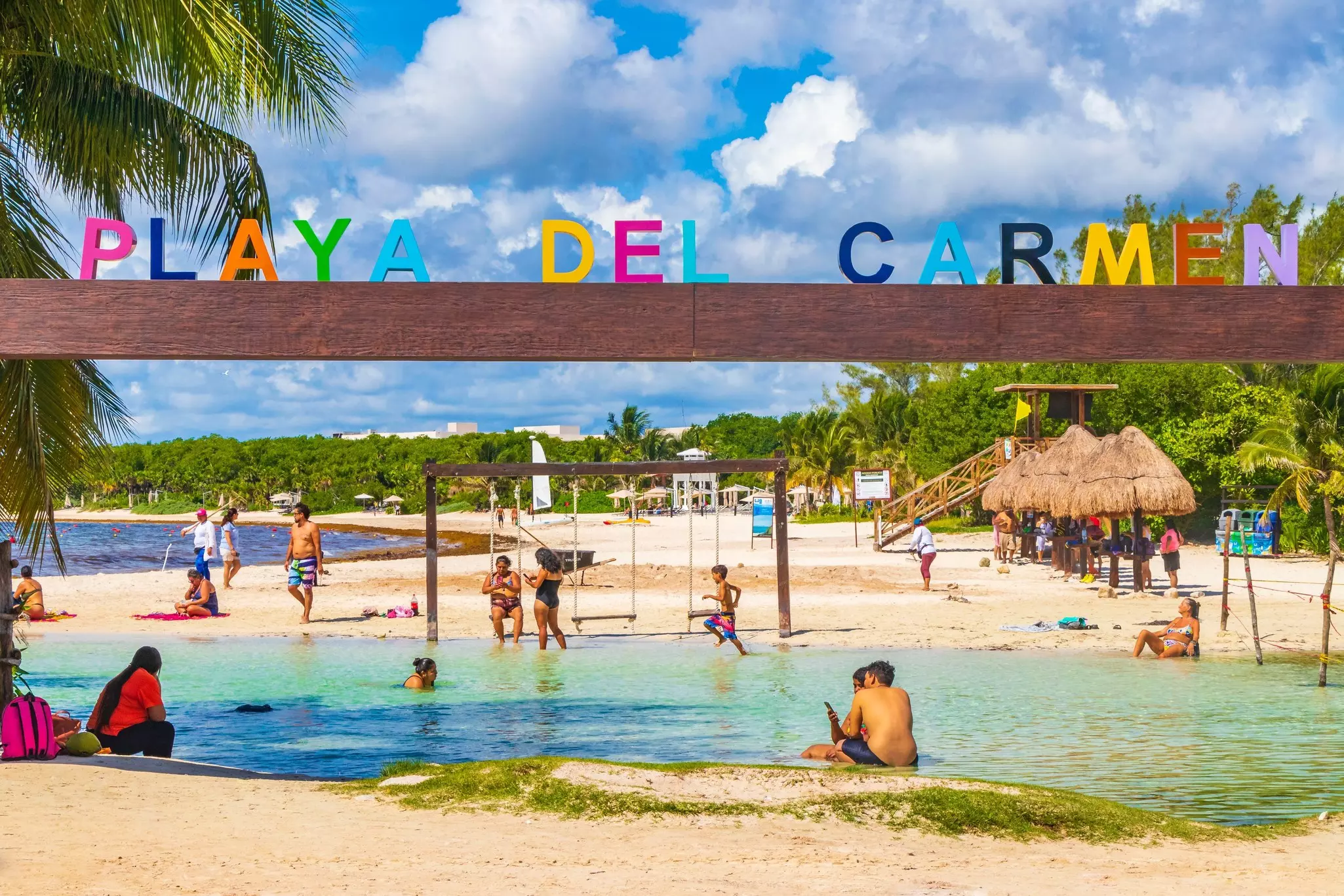 Kids playing beneath a Playa del Carmen colorful sign at the beach. 