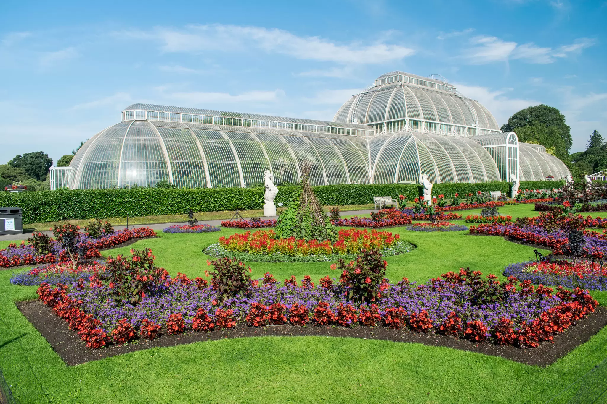 A huge glasshouse in manicured gardens with pink flowers in flowerbeds