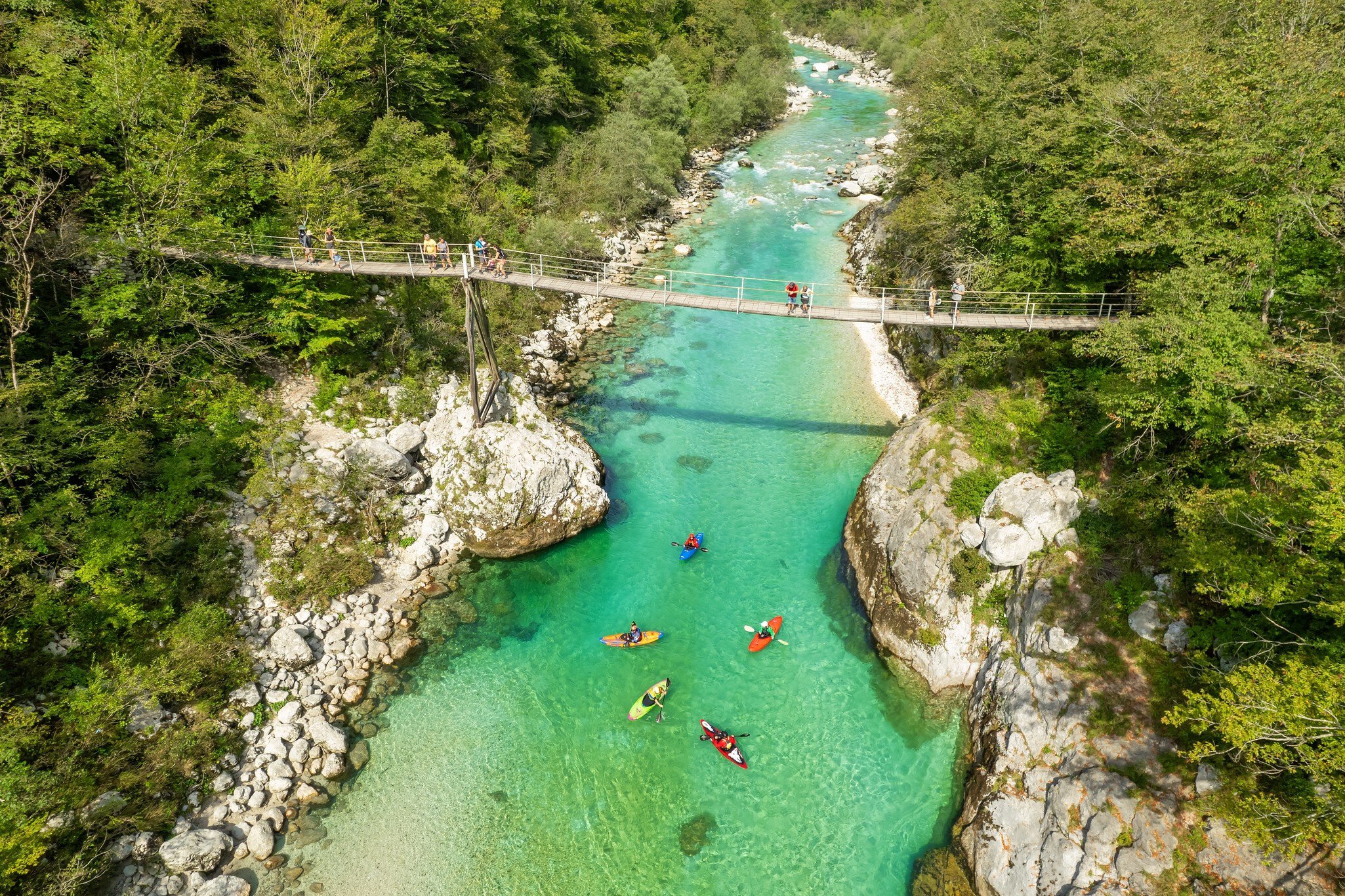 A suspension bridge spans the emerald waters of the Soca River in Slovenia, aerial view. This spot is a favored destination for kayaking and trekking in Slovenia.