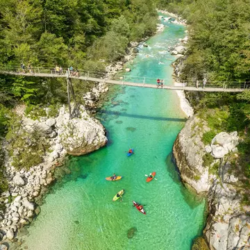 A suspension bridge spans the emerald waters of the Soca River in Slovenia, aerial view. This spot is a favored destination for kayaking and trekking in Slovenia.