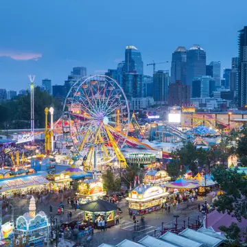 A fun fair with a Ferris wheel lit up at night at a busy event in a city.