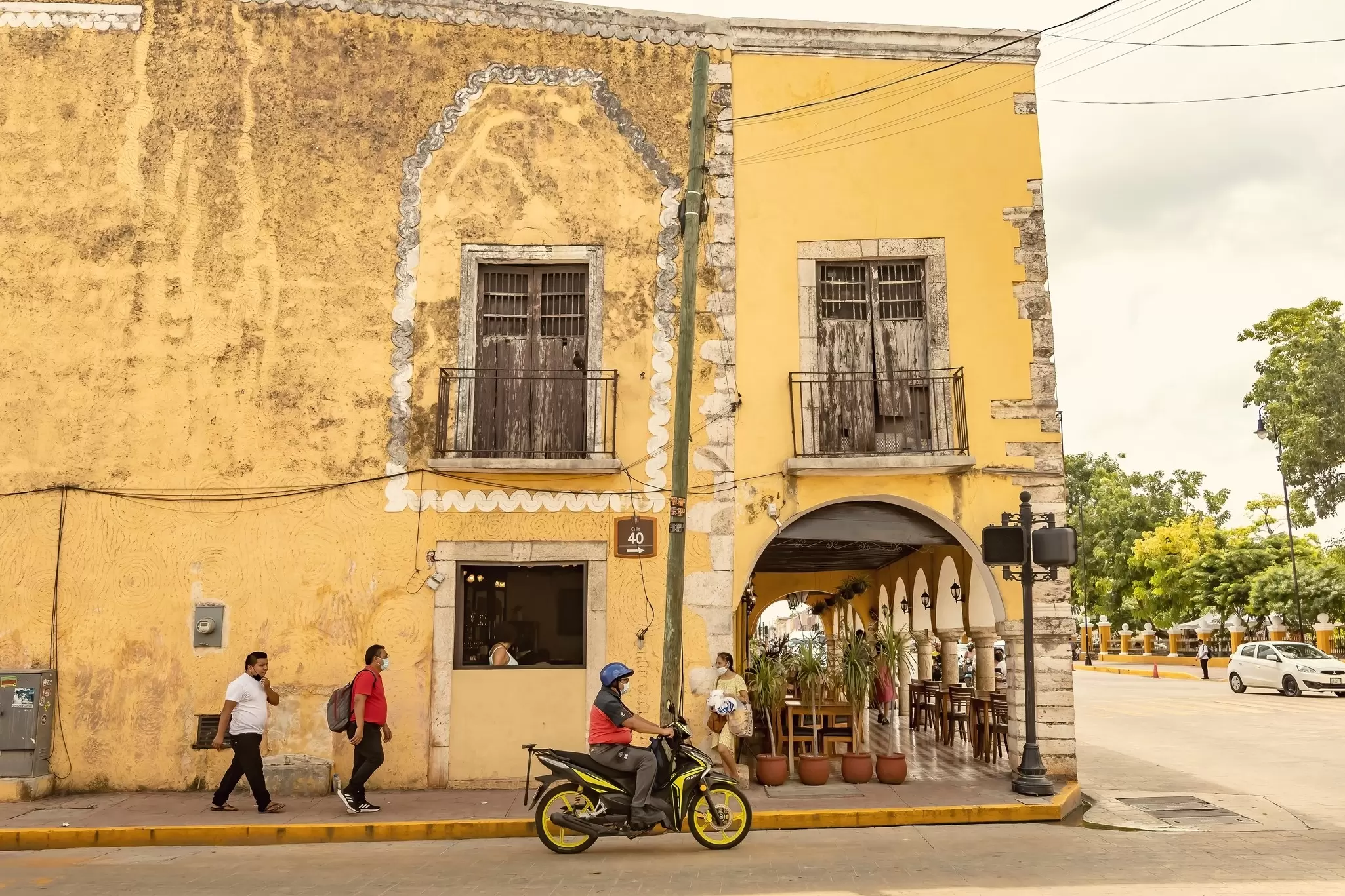 Pedestrians and a motorcyclist are pictured in front of a yellow-painted, colonial-era building in Valladolid, Yucatán Peninsula, Mexico