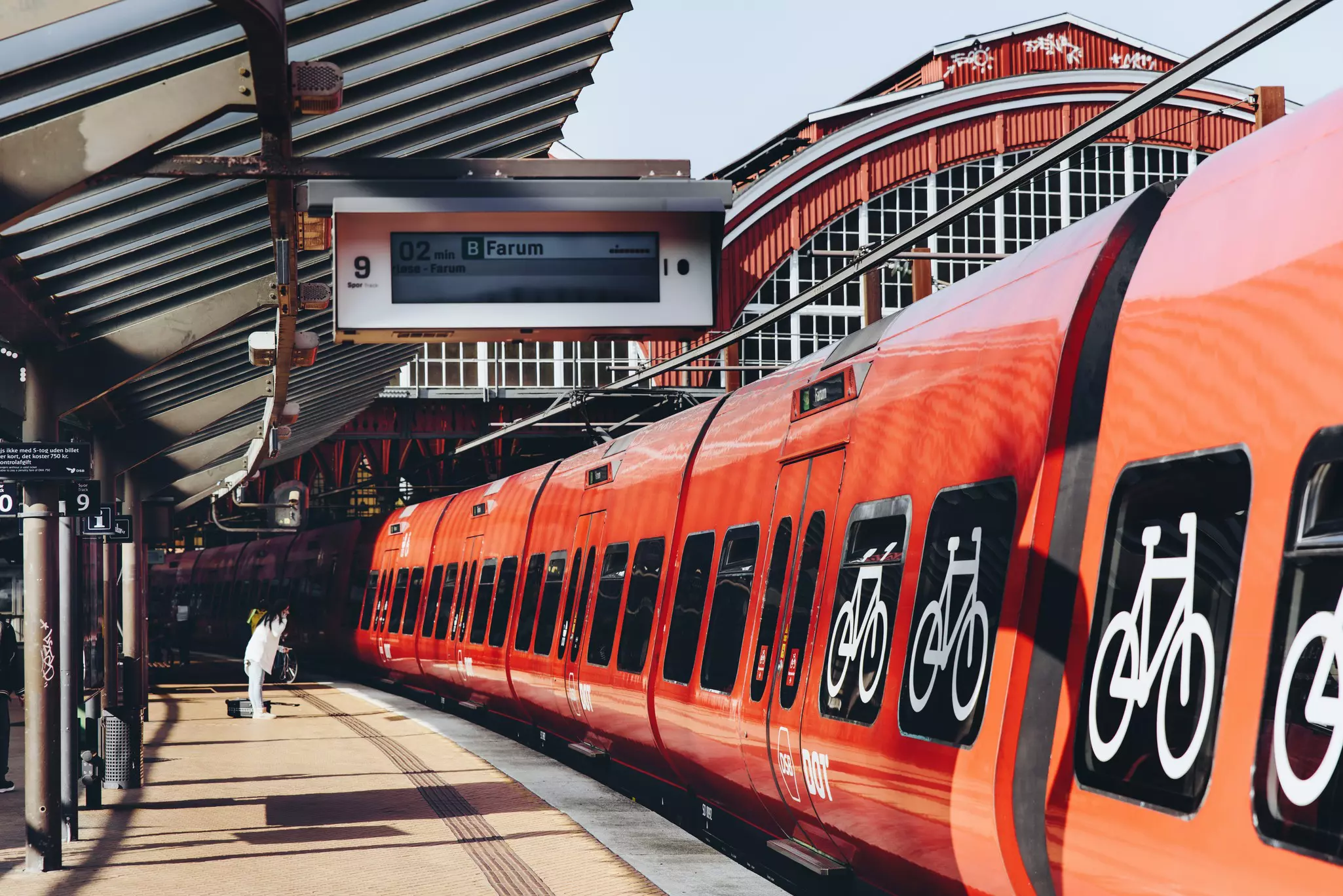 Close-up of red Metro train with bicycle symbols painted on the windows and a passenger on the platform in the distance.