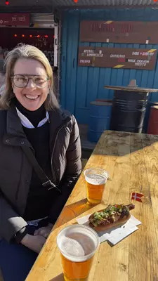 Close-up of a smiling woman at a table with an open-faced sandwich and glasses of beer.