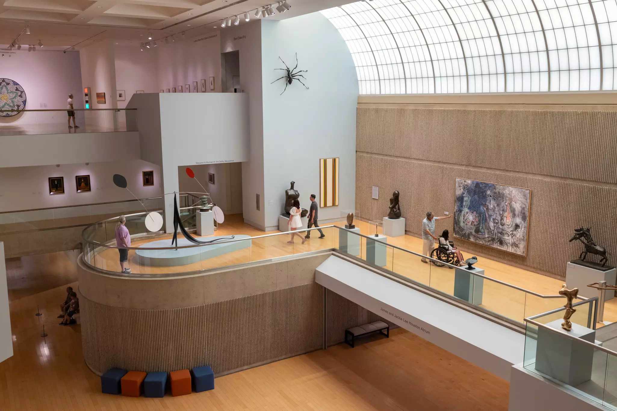 Patrons visit the Palm Springs Art Museum's main hall, where sculptures and paitings line the walls and sunlight comes down through a curved glass skylight.