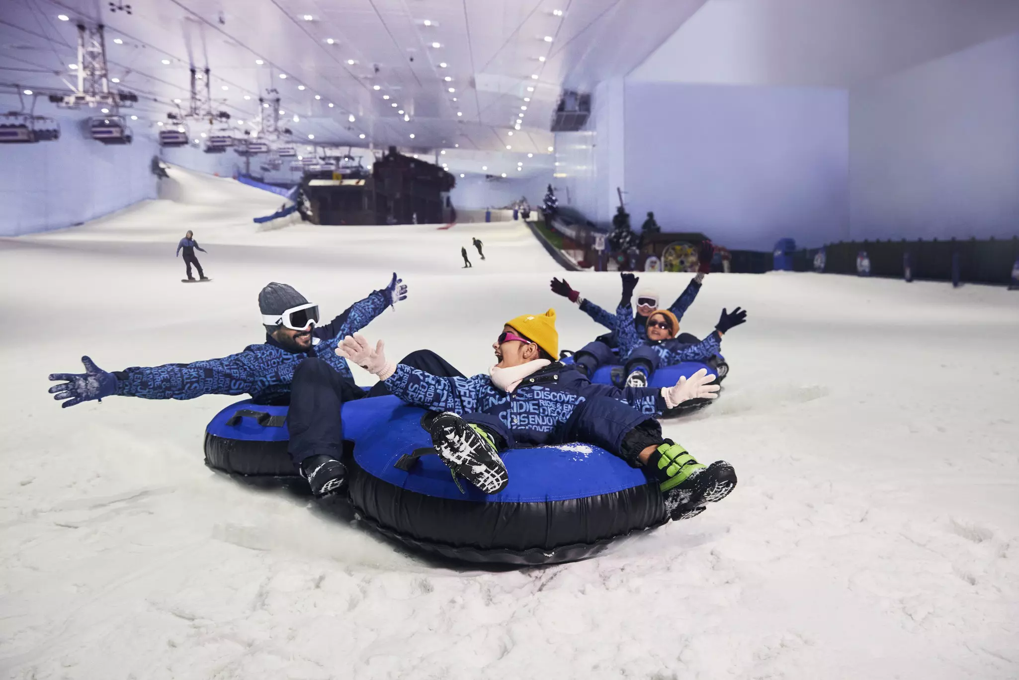 Four people riding sleds down an indoor snowy mountain.