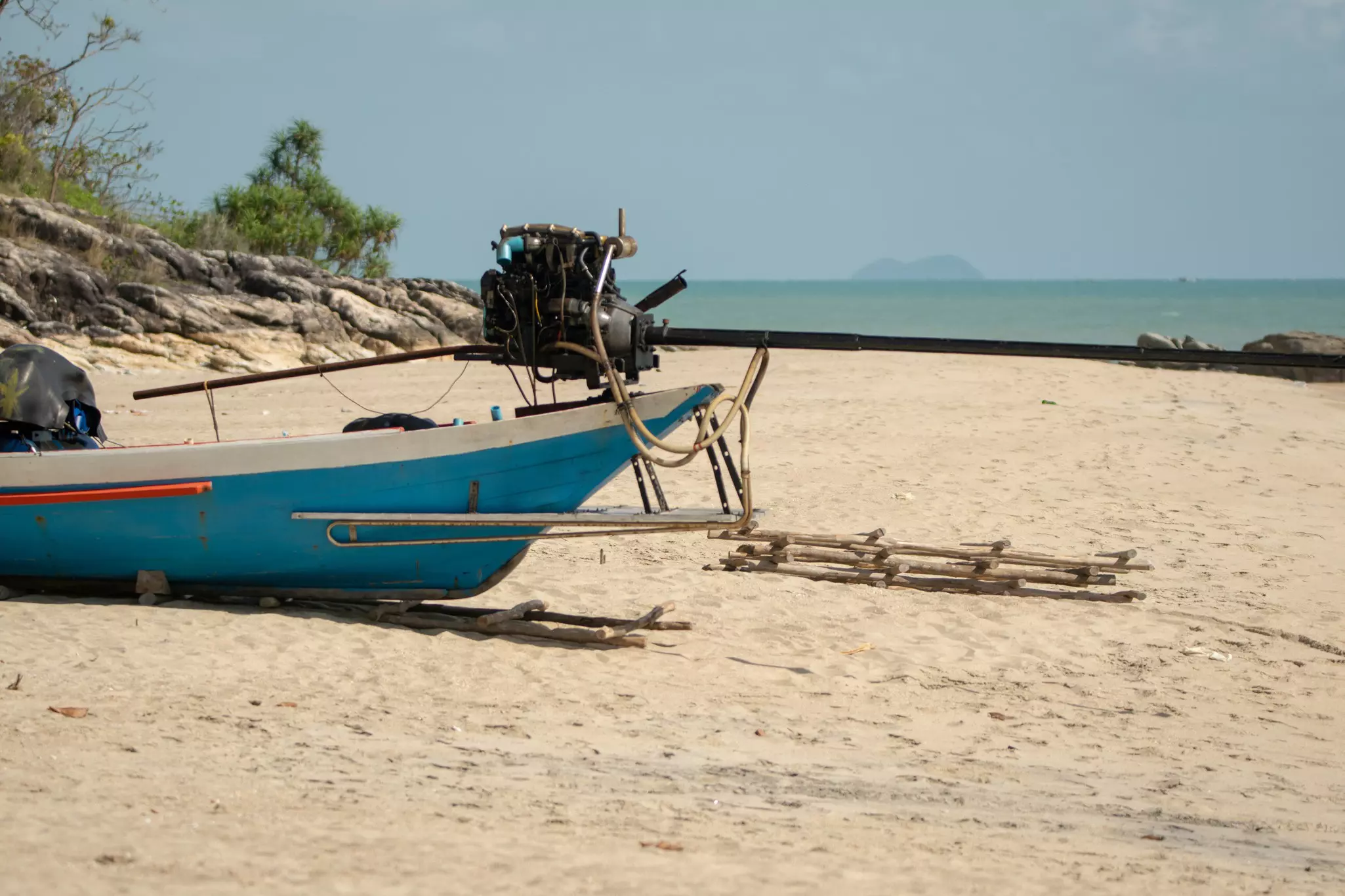 A blue fishing boat is pulled onto the sand of a wide beach, its outboard motor folded up over the stern