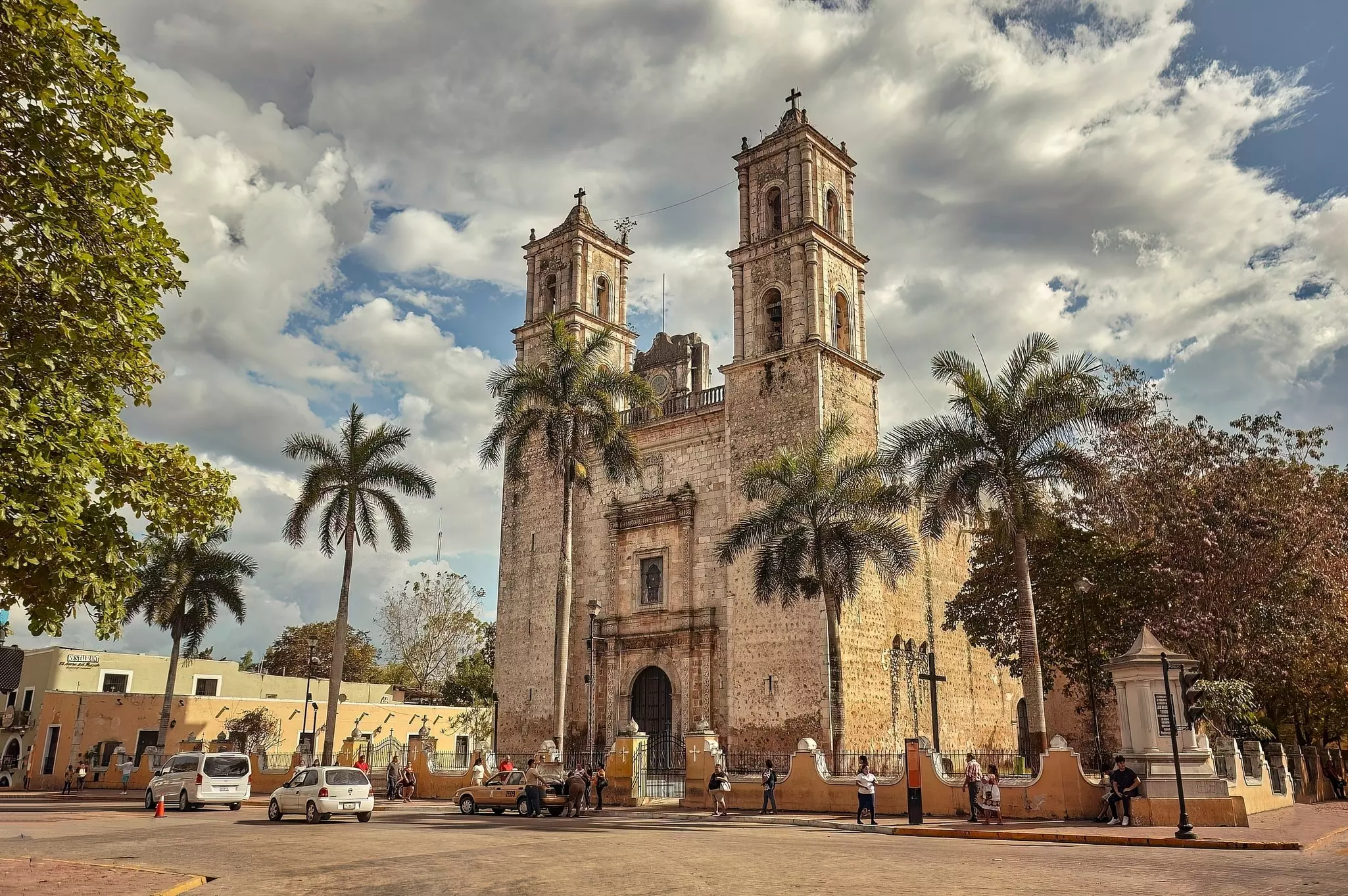 A narrow, tall church with two bell towers photographed from a plaza across the street. Palm trees and taxis are seen in front of the church.