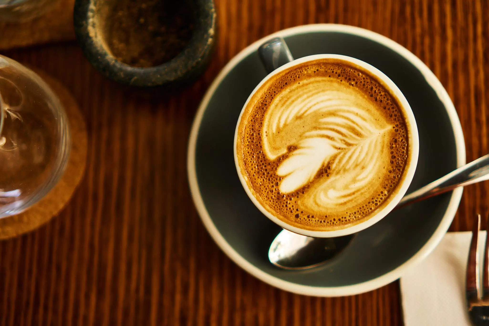 A coffee in a cup on a saucer with a slightly frothy milky top.